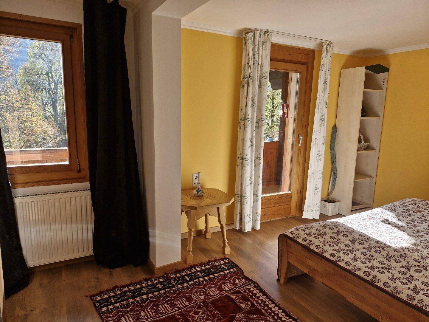 Gemütliches Schlafzimmer mit gelben Wänden, Holzboden und direktem Zugang zum Balkon.