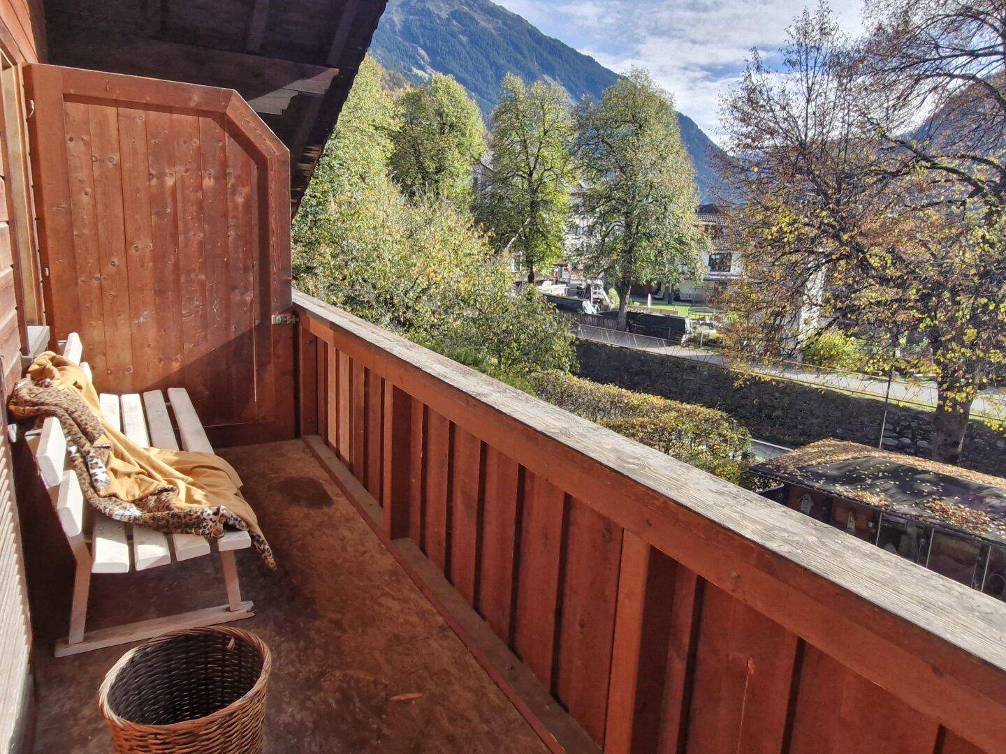 Holzbalkon mit Sitzbank und Blick auf die grüne Umgebung sowie die umliegenden Berge.