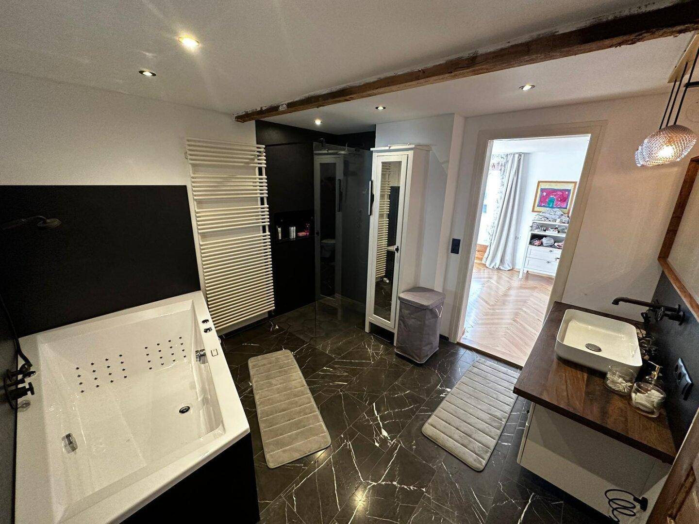 Modernes Badezimmer mit dunklen Marmorfliesen, großer Badewanne und separater Duschkabine.