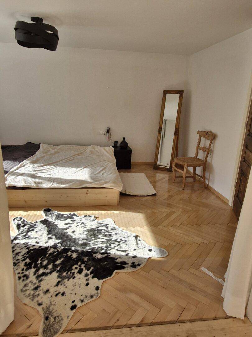 Helles Schlafzimmer mit Holzbett, Fischgrätparkett, Kuhfellteppich und großem Spiegel.