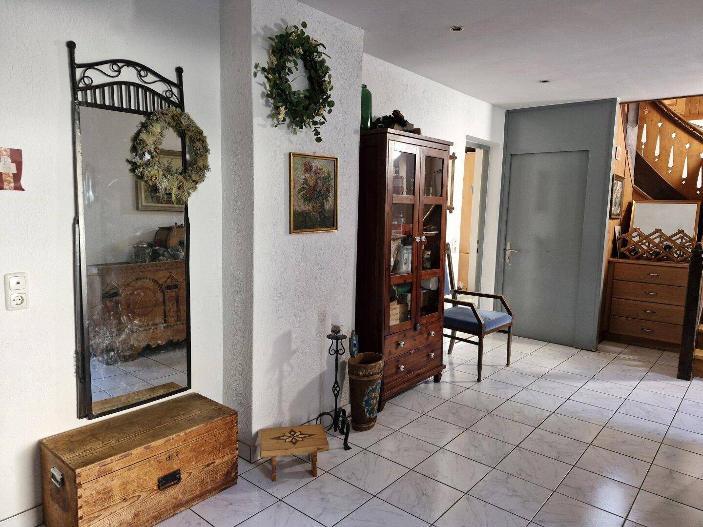 Eingangsbereich mit Fliesenboden, großem Spiegel und antiken Holzmöbeln, Treppe im Hintergrund.