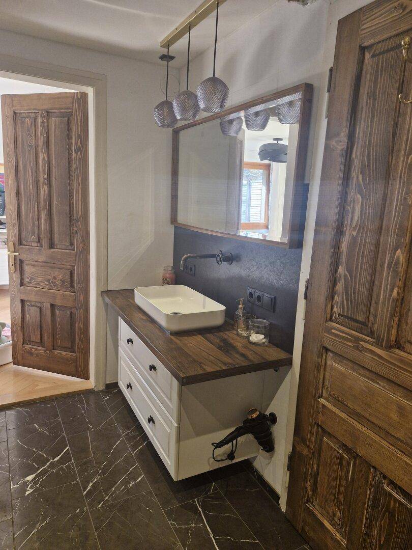 Badezimmer-Waschtisch mit Holzplatte, Aufsatzwaschbecken und dunklem Marmorfliesenboden.