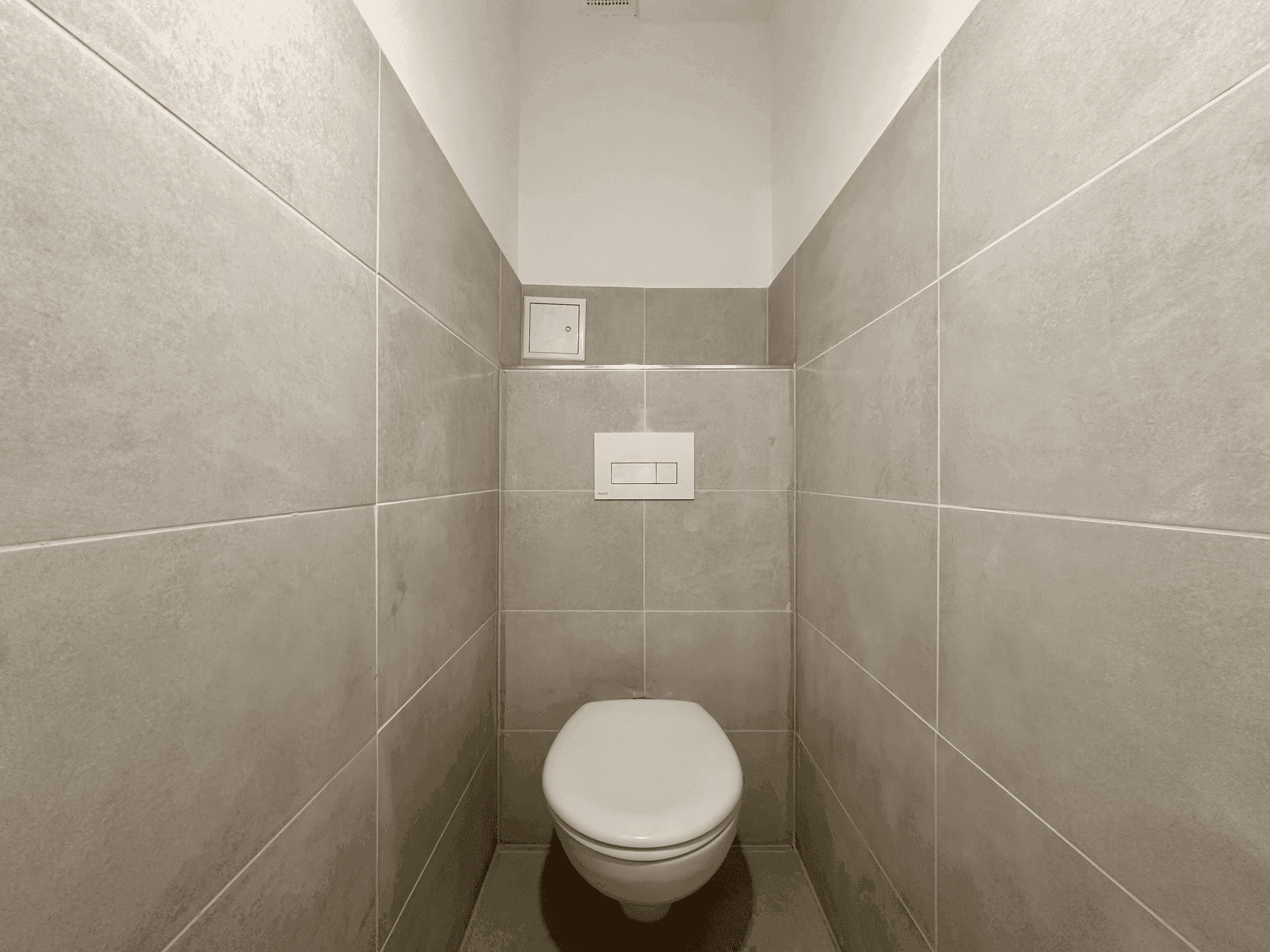 Separates WC mit hellgrauen Fliesen und einer wandhängenden Toilette, sauber und funktional.