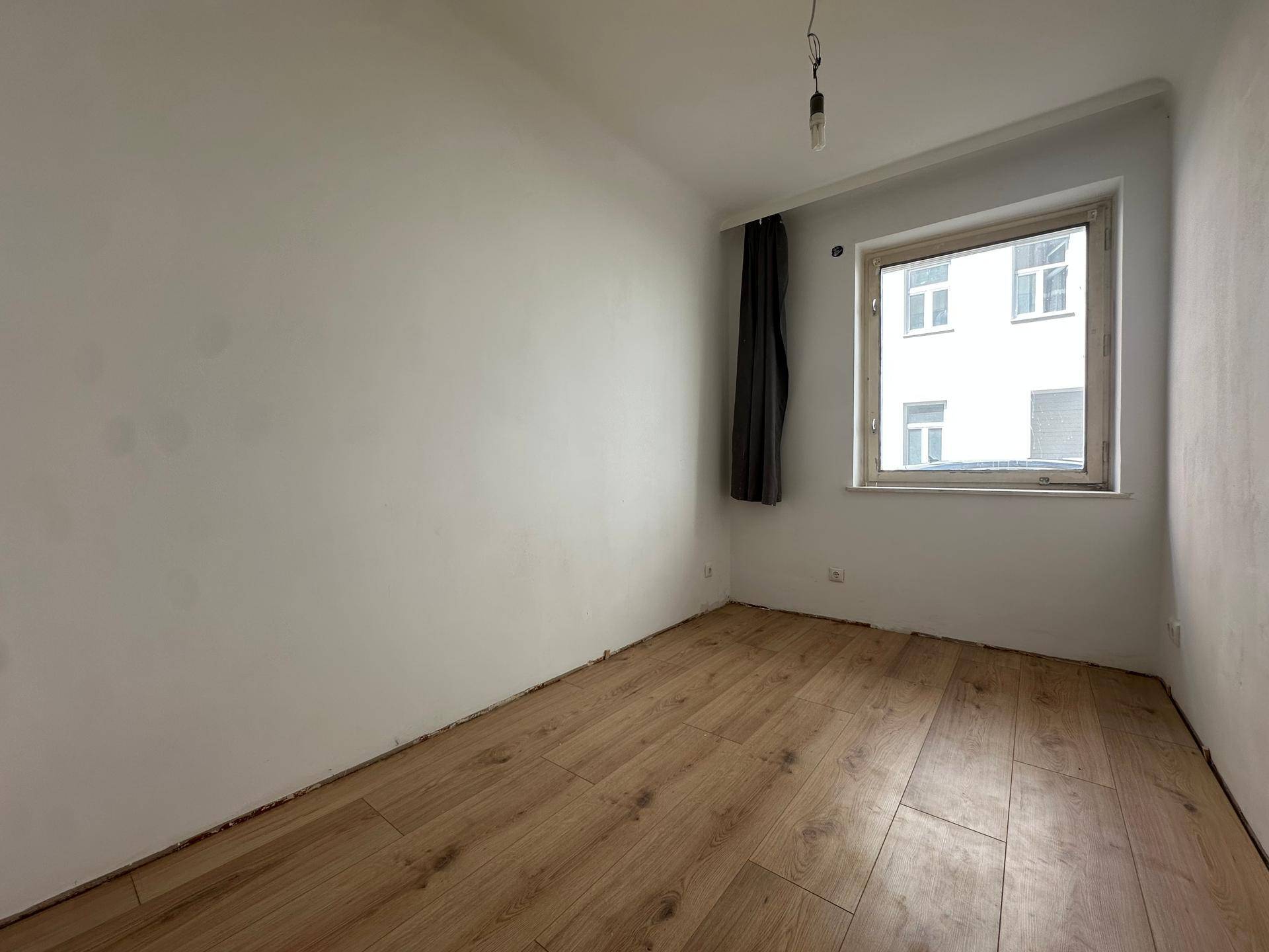 Leerer Raum mit hellem Laminatboden, weißen Wänden und einem Fenster, bereit zur individuellen Gestaltung.