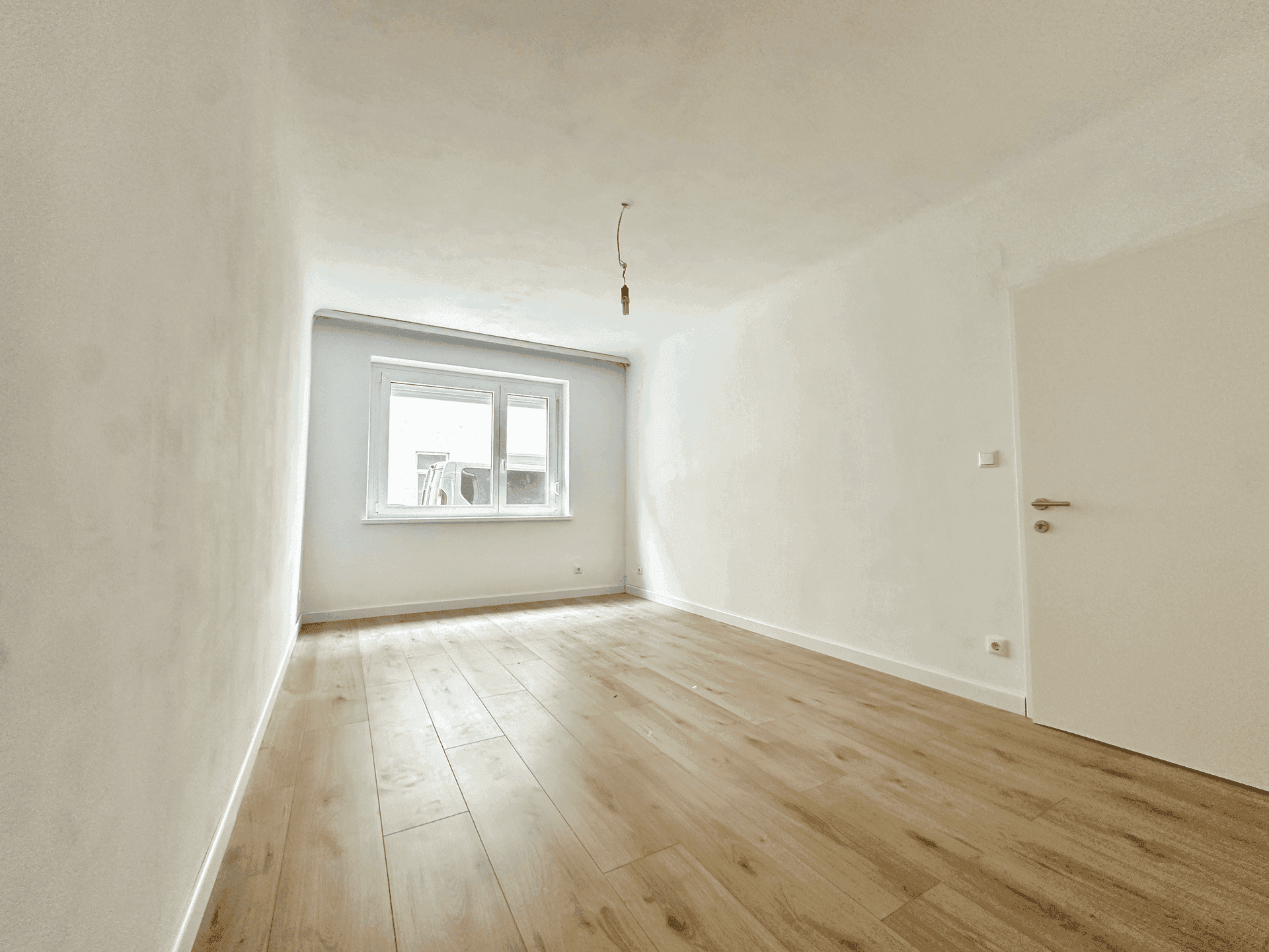 Heller, leerer Raum mit neuem Holzboden und einem Fenster, bereit zur individuellen Gestaltung.