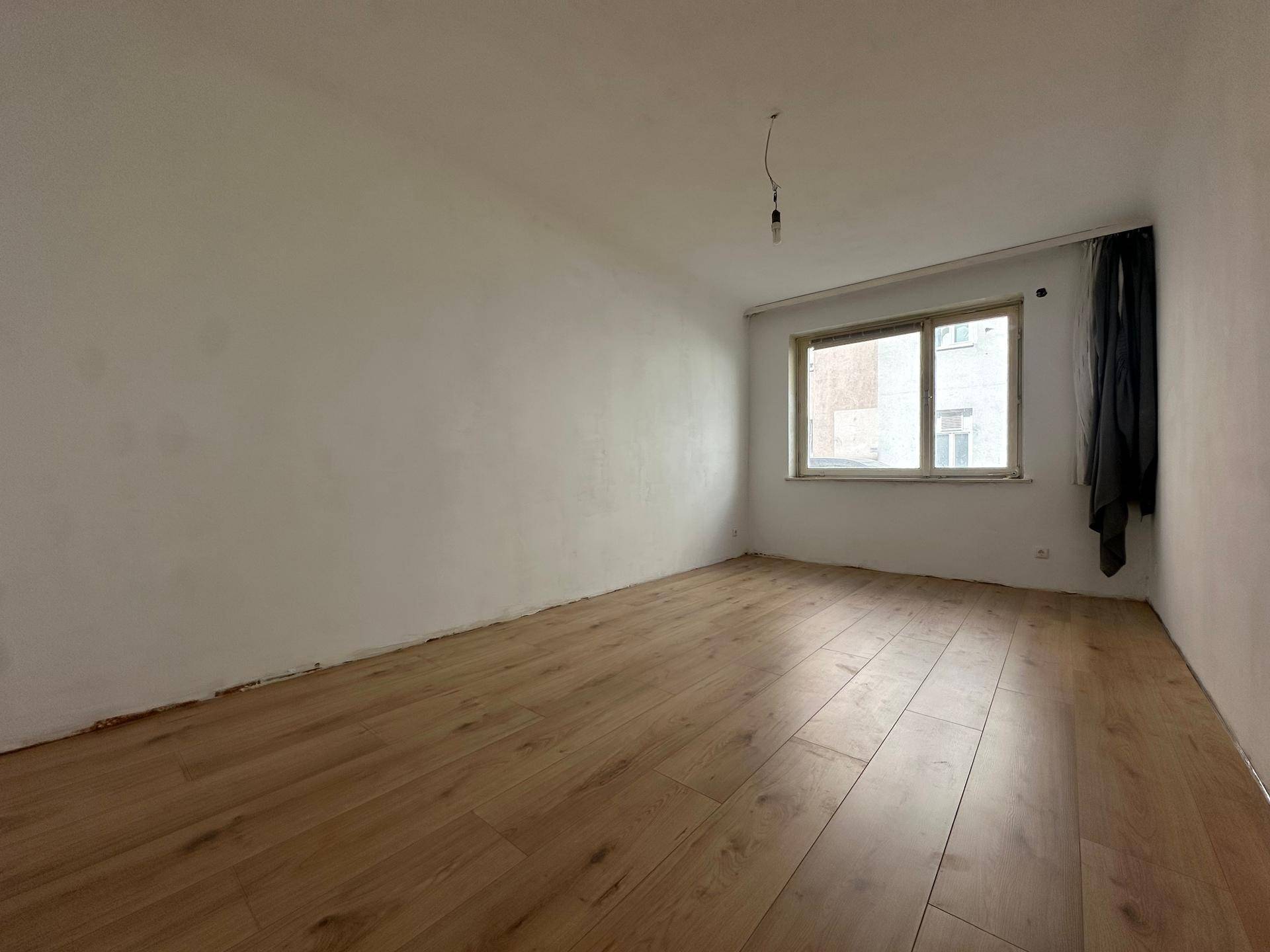 Heller, leerer Raum mit Laminatboden und einem Fenster, das Tageslicht hereinlässt.