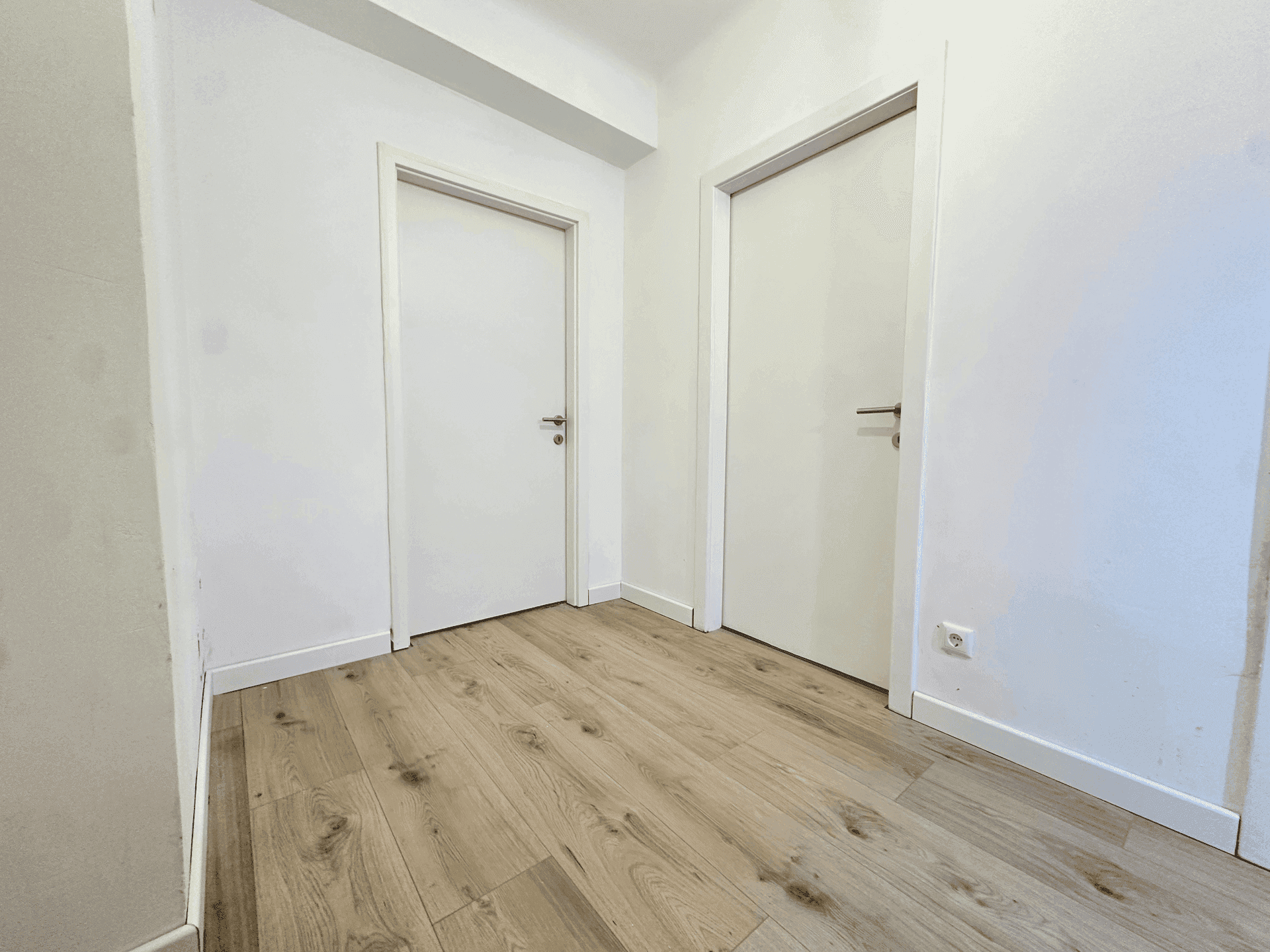 Heller Flur mit Holzboden und zwei weißen Türen, verbindet die verschiedenen Räume der Wohnung.