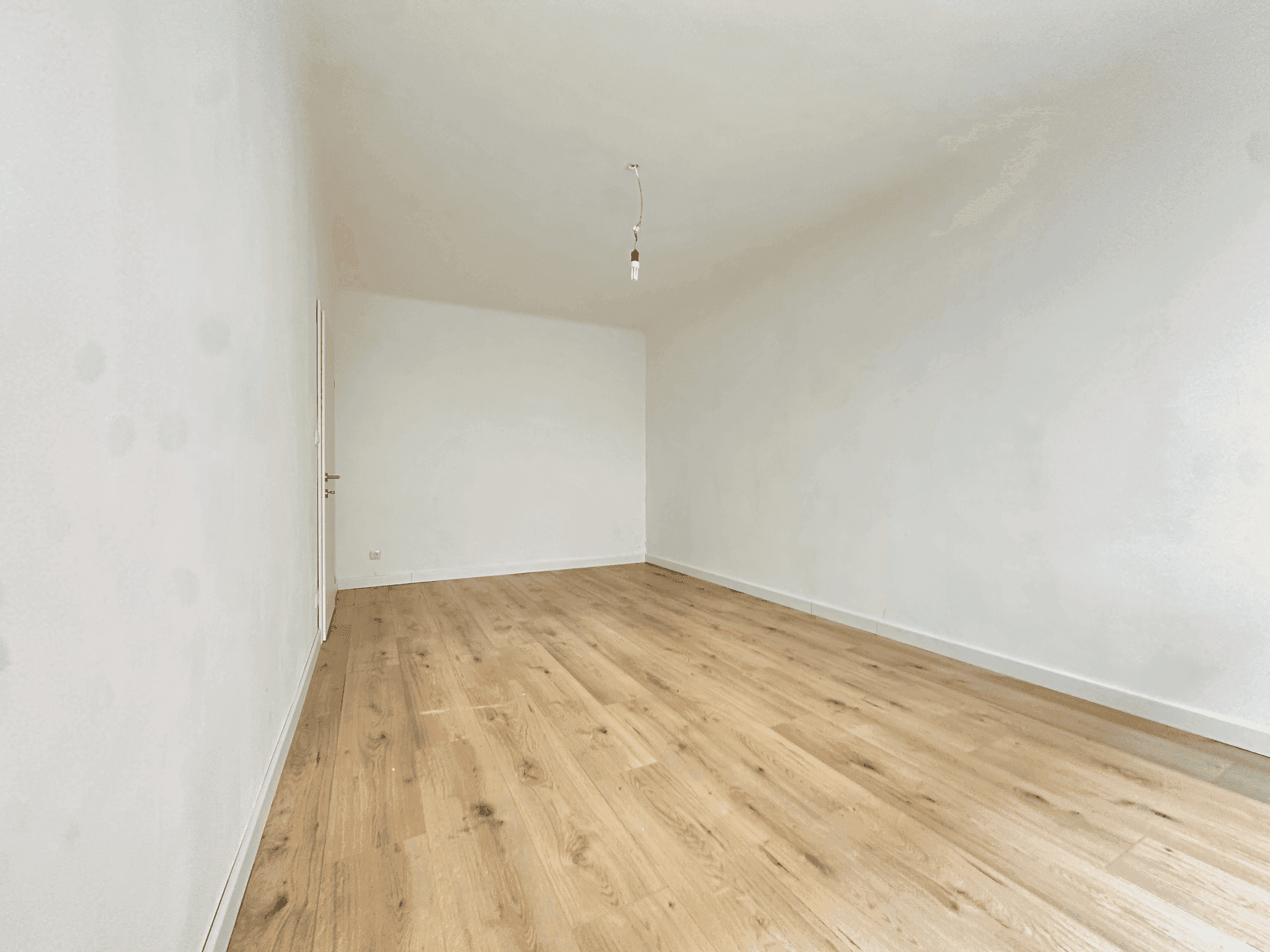 Geräumiger, leerer Raum mit hellem Holzboden und weißen Wänden, ideal für Wohn- oder Schlafbereich.