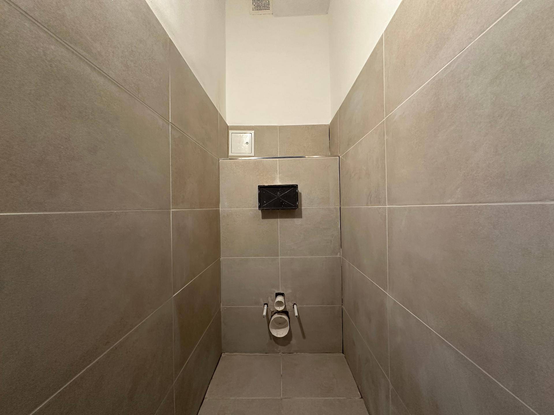 Kleiner Raum, wahrscheinlich eine Gästetoilette, mit grauen Fliesen an Wänden und Boden.
