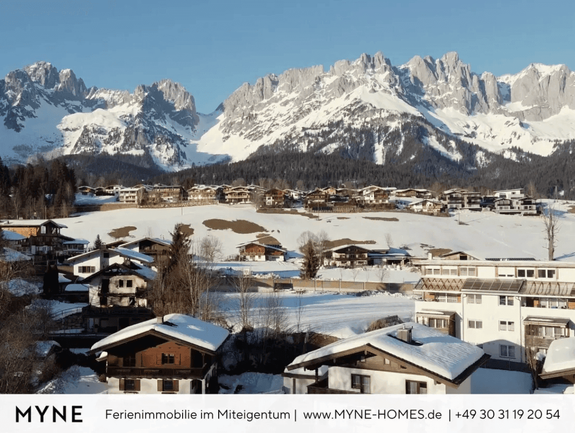 Idyllische Winterlandschaft mit einem verschneiten Dorf und majestätischem Bergpanorama im Hintergrund.