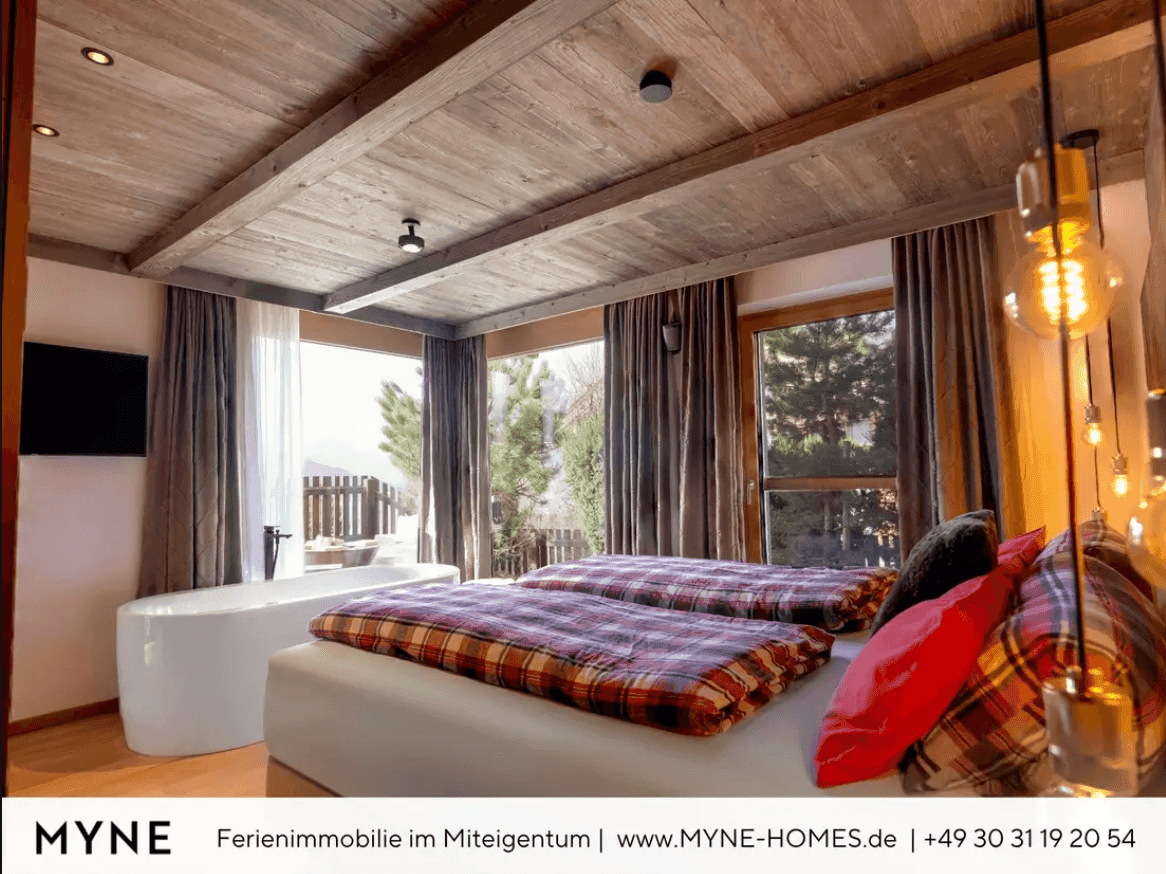 Geräumiges Schlafzimmer mit freistehender Badewanne, Holzbalkendecke und großzügigen Fenstern.