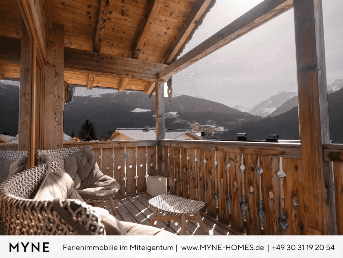 Gemütlicher Holzbalkon mit Sitzgelegenheiten und weitem Blick auf die verschneite Bergwelt.