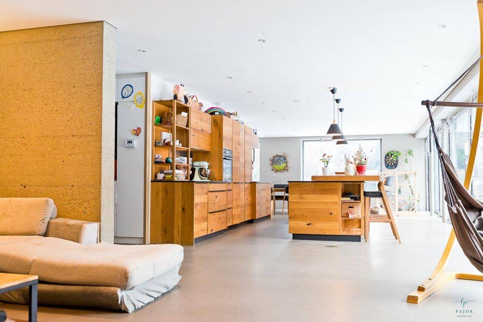 Heller Wohnbereich mit bequemer Couch, offener Küche und großen Fenstern zum Garten.