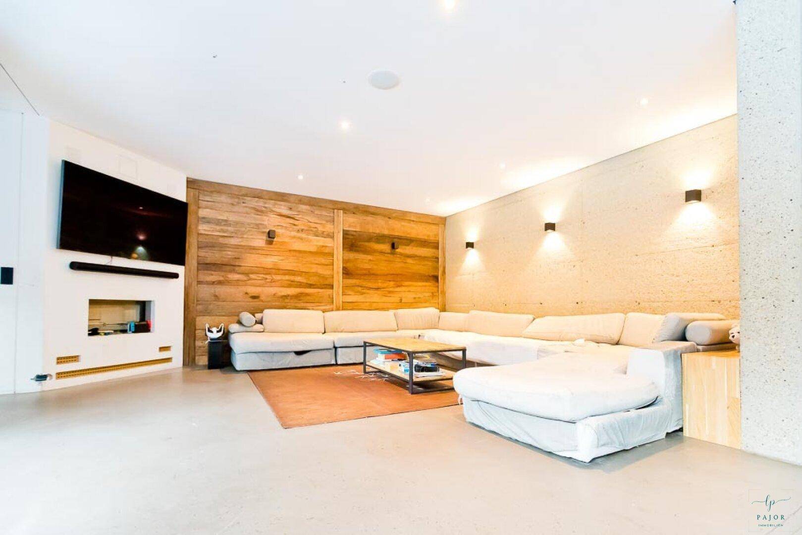Gemütlicher Wohnbereich mit großer Eckcouch, Holzwand und integriertem Kamin sowie TV-Bereich.