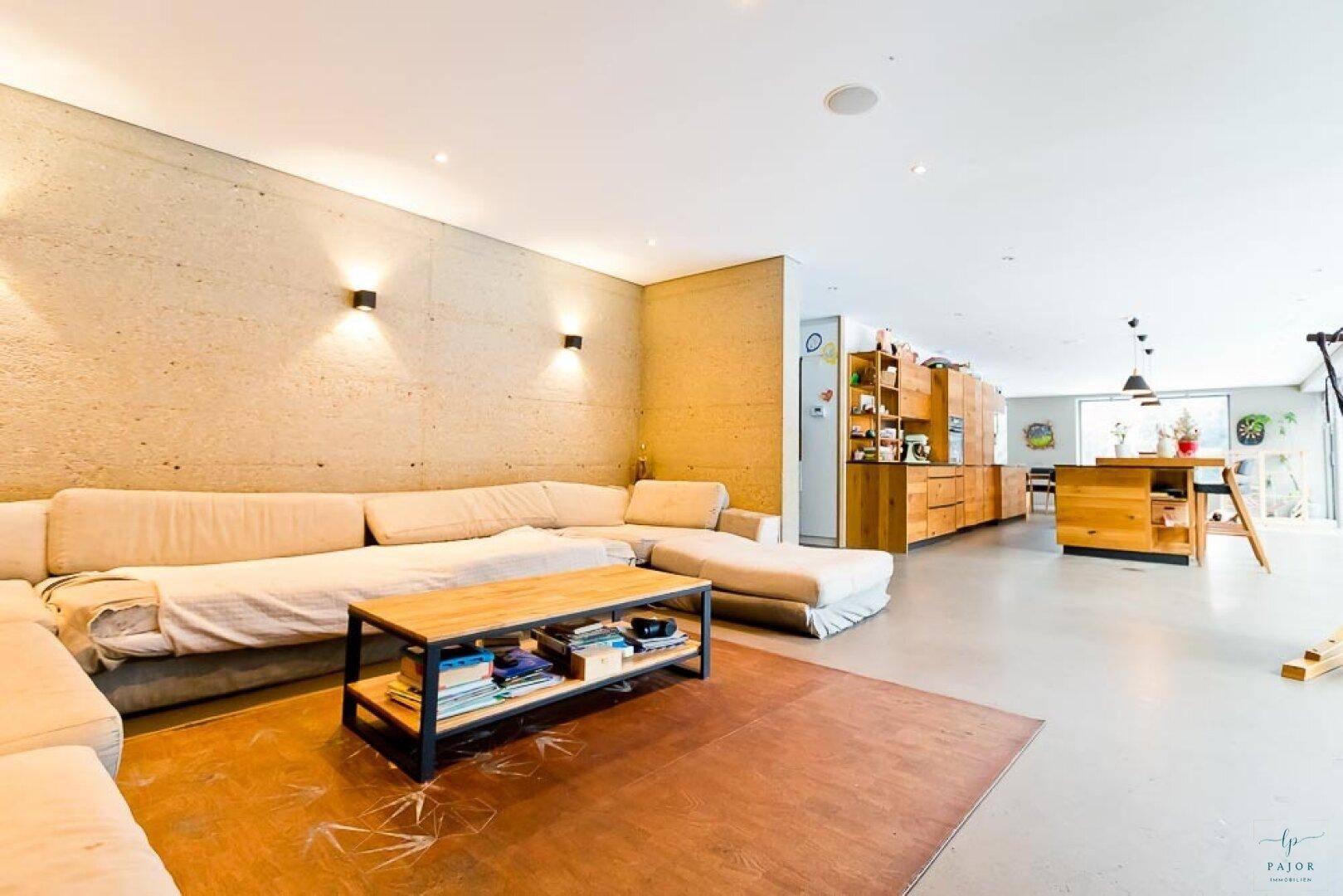 Geräumiger Wohnbereich mit beiger Couch, moderner Einrichtung und offenem Übergang zur Küche.