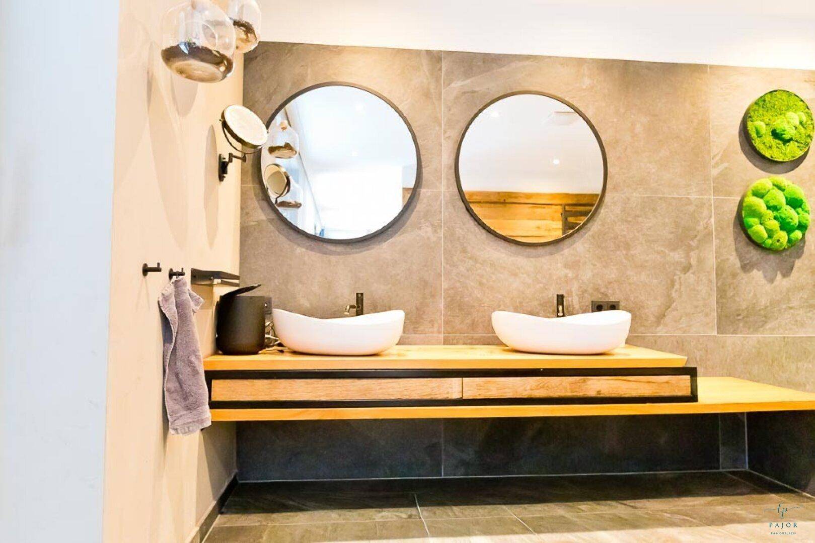 Doppelwaschbecken auf einer Holzplatte mit runden Spiegeln in einem modernen Badezimmer.