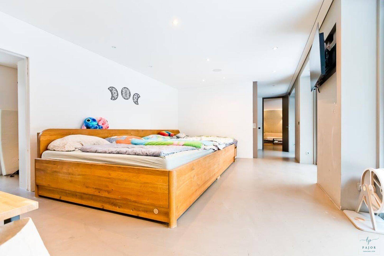 Geräumiges Schlafzimmer mit Holzbett, weißer Einrichtung und einem an der Wand montierten Fernseher.
