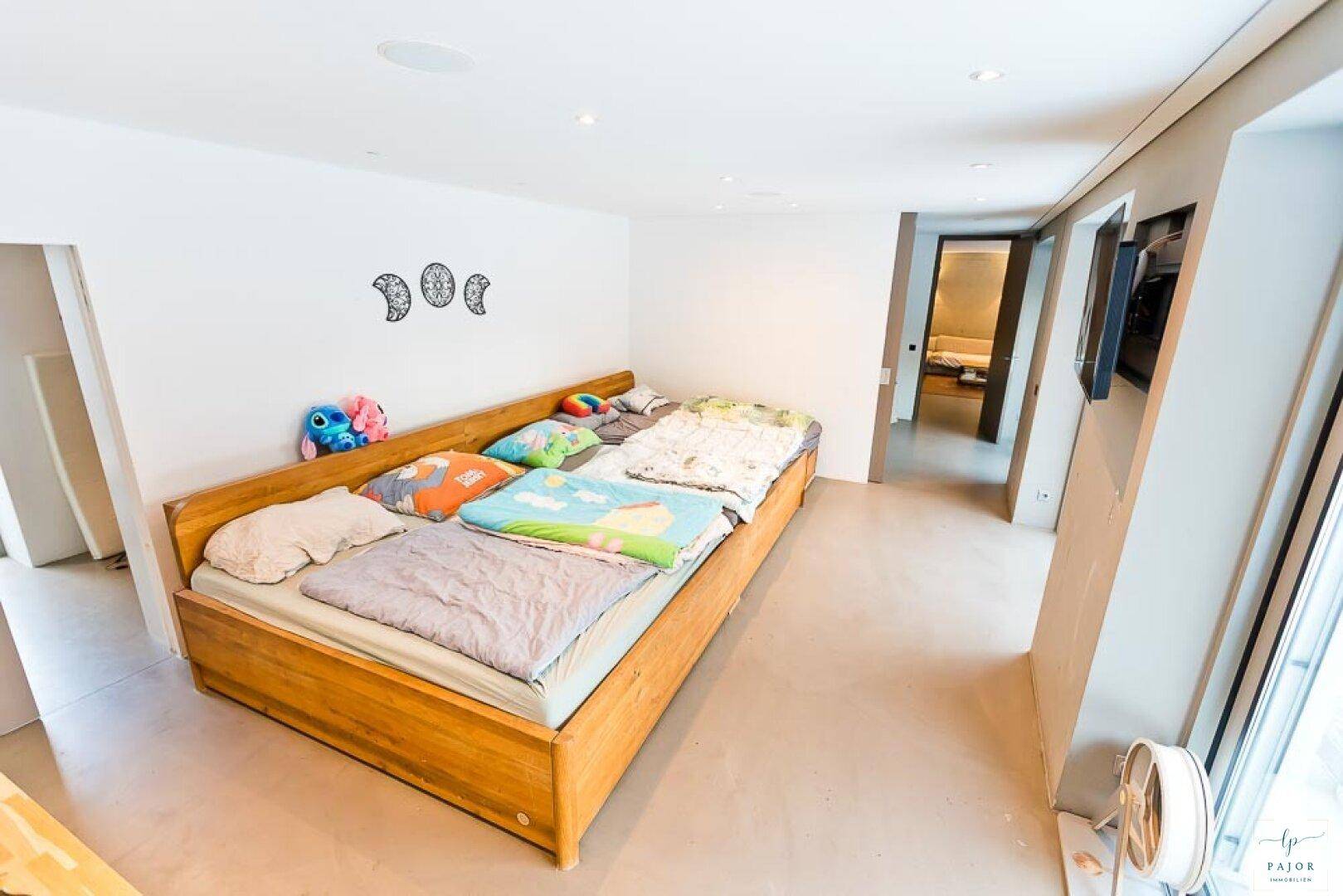 Helles Schlafzimmer mit mehreren Betten, Holzelementen und viel Tageslicht durch große Fenster.