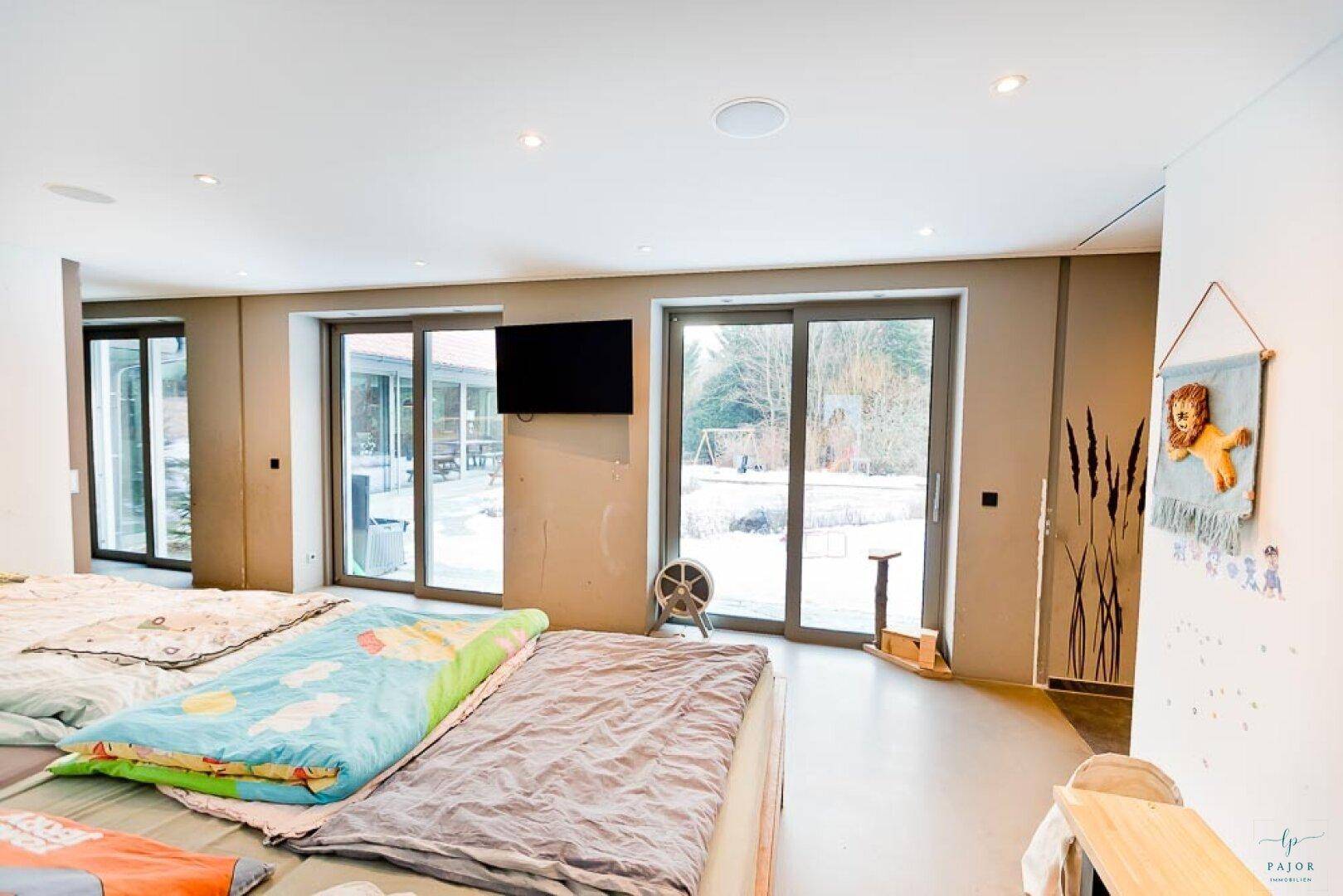 Großes Schlafzimmer mit mehreren Betten und breiten Glasschiebetüren zum verschneiten Garten.