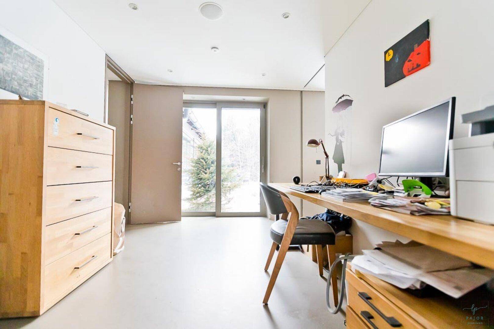 Helles Arbeitszimmer mit Holzschreibtisch und großer Schiebetür, die ins Freie führt.