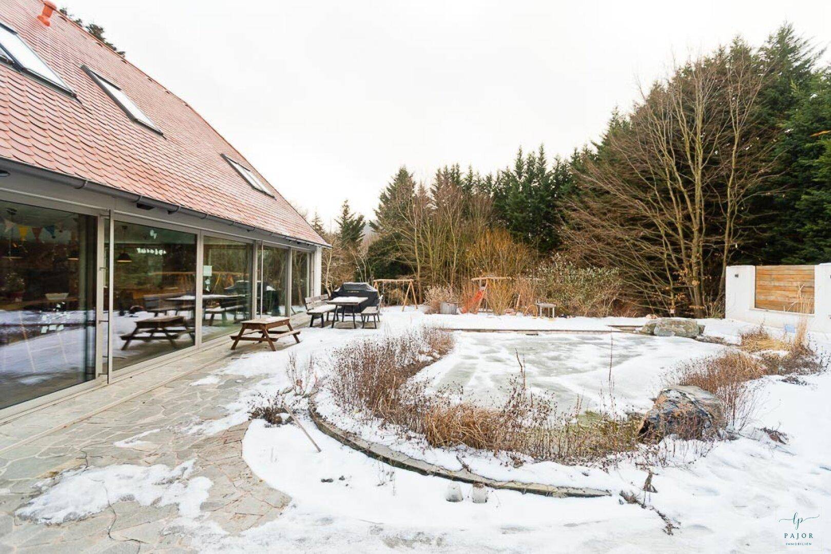 Winterlicher Gartenbereich mit Terrasse, gefrorenem Teich und Blick auf das moderne Haus.