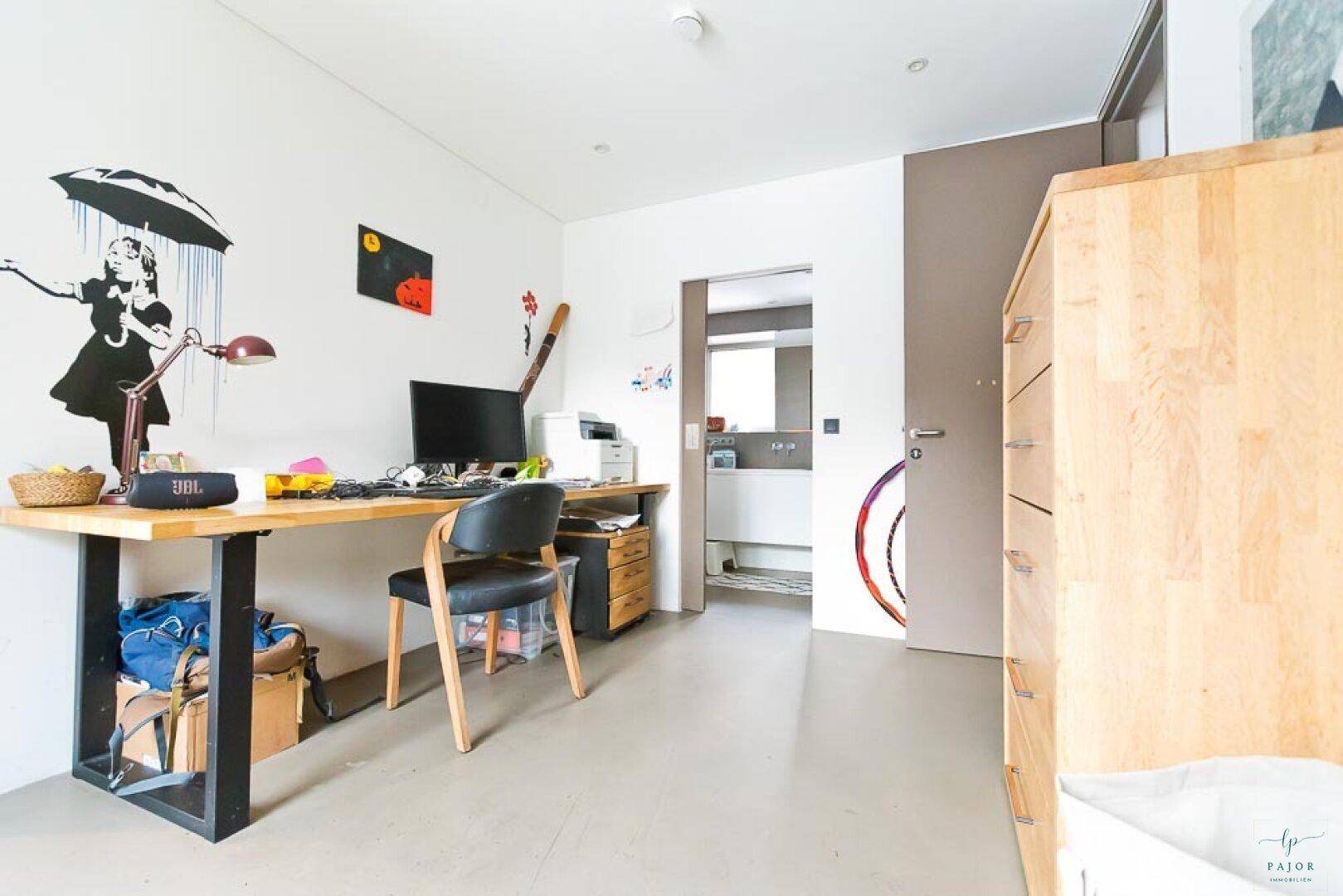 Modernes Arbeitszimmer mit Schreibtisch, Computer und Zugang zu einem Badezimmer.