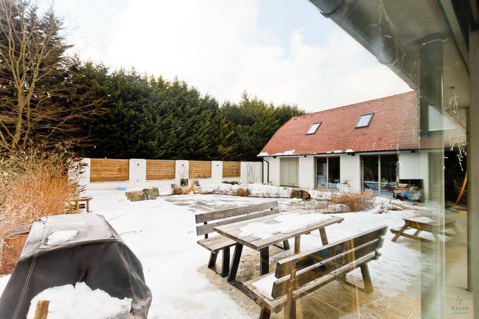 Winterliche Terrasse mit Holzbänken und Blick auf das Haus und den verschneiten Garten.