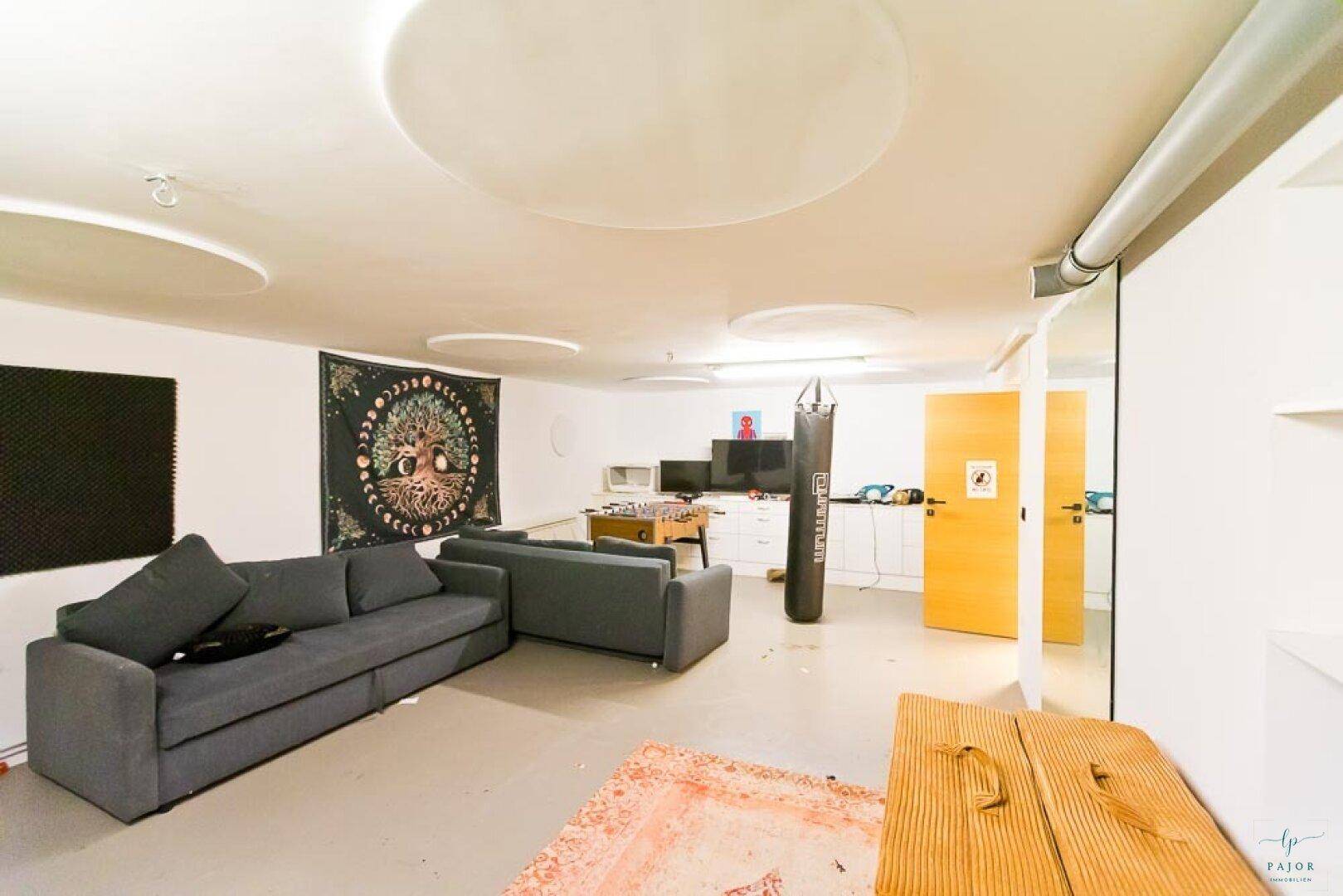 Geräumiger Kellerraum, eingerichtet als Freizeitbereich mit Sofa und Sportgeräten.