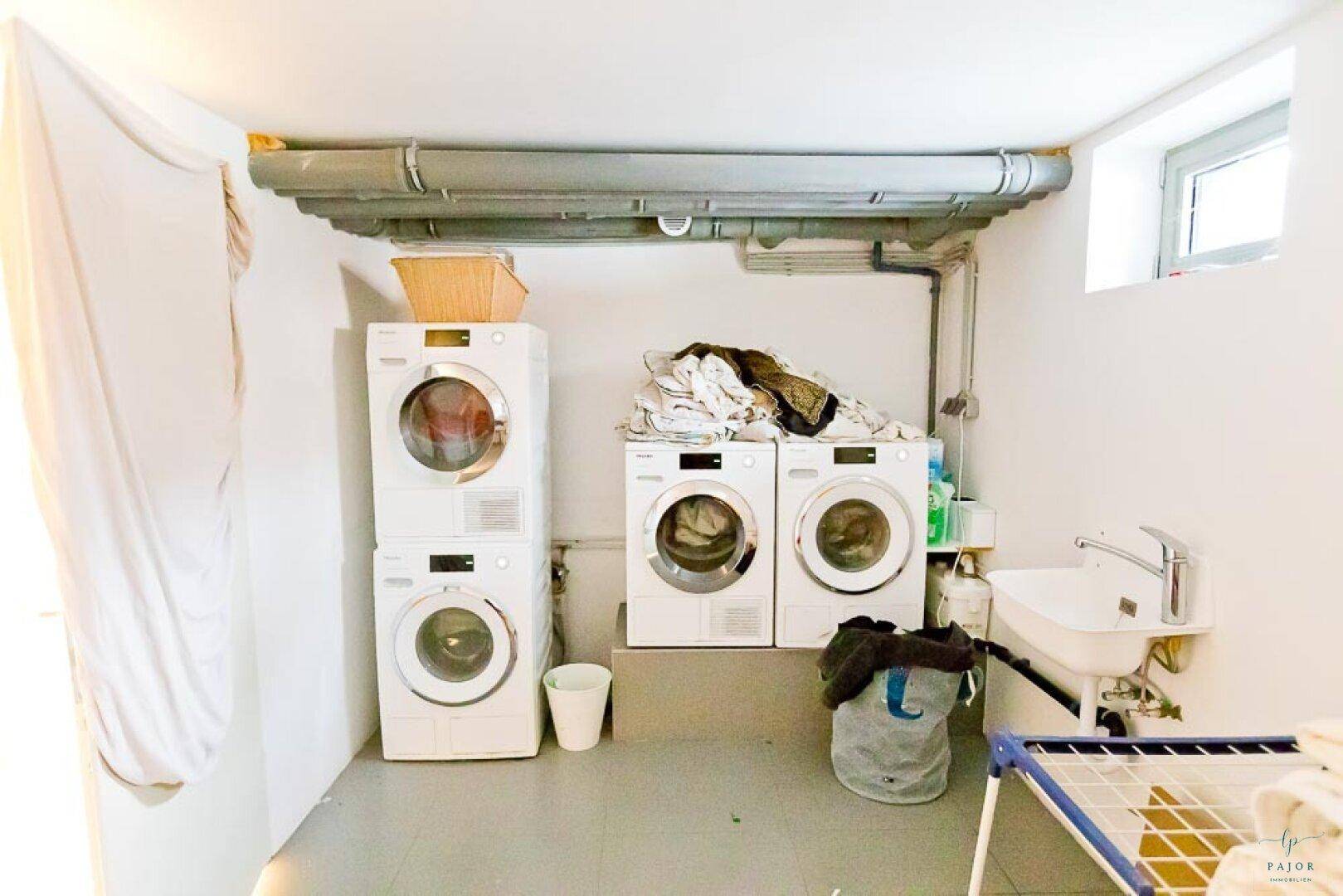 Funktionale Waschküche im Keller mit mehreren Waschmaschinen, Trockner und Waschbecken.