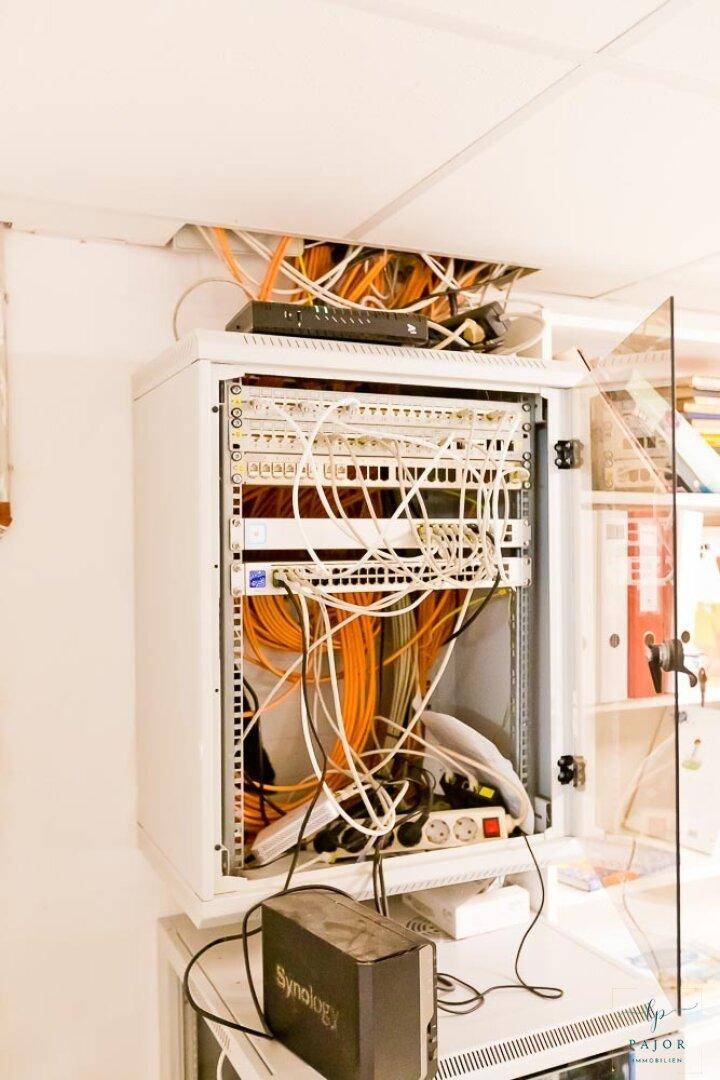 Serverschrank mit umfangreicher Verkabelung und Netzwerkgeräten in einem Technikraum.