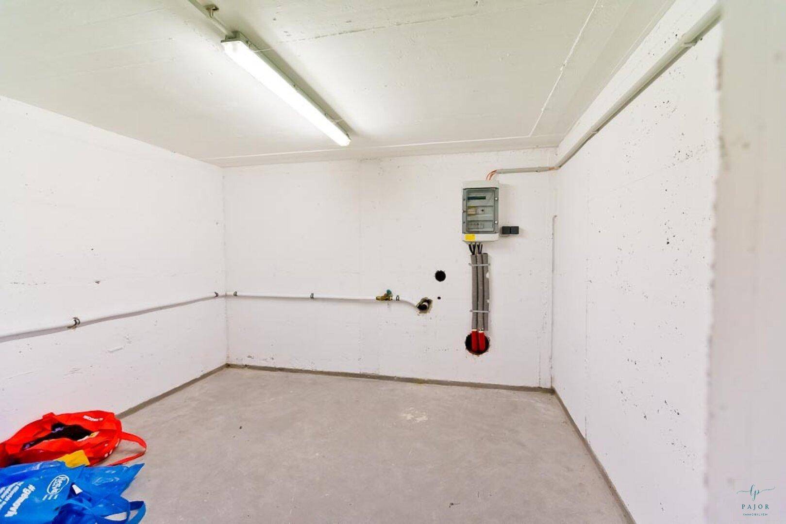 Leerer Raum mit Betonboden, weiß gestrichenen Wänden und einem Sicherungskasten.