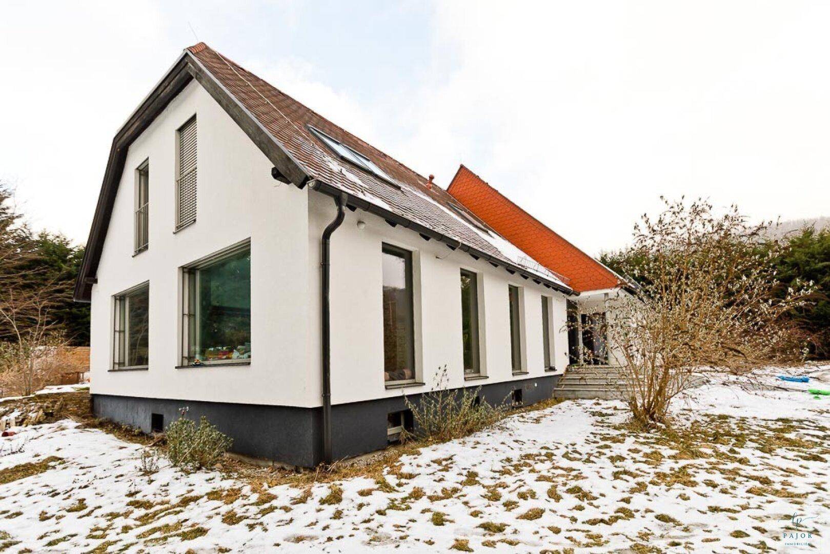 Ansicht des weißen Hauses mit rotem Ziegeldach und großen Fenstern im winterlichen Garten.