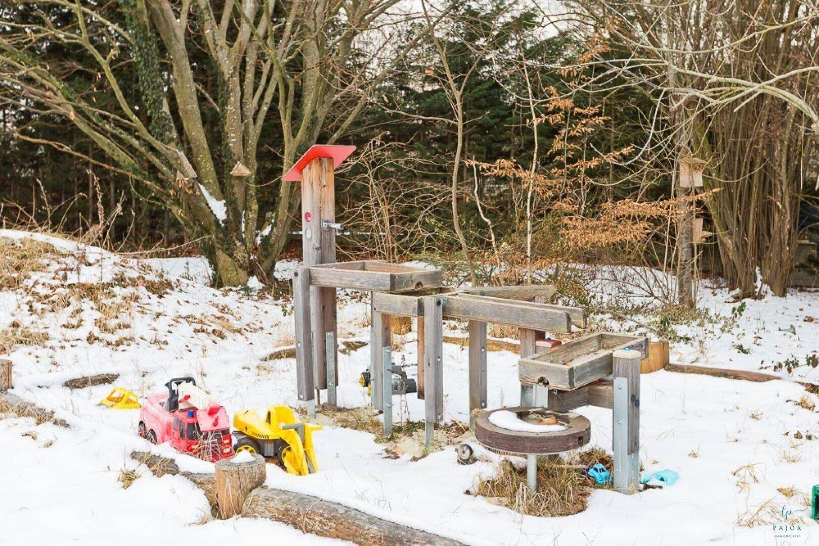 Detailansicht eines hölzernen Wasserspielplatzes mit Spielzeug im verschneiten Garten.