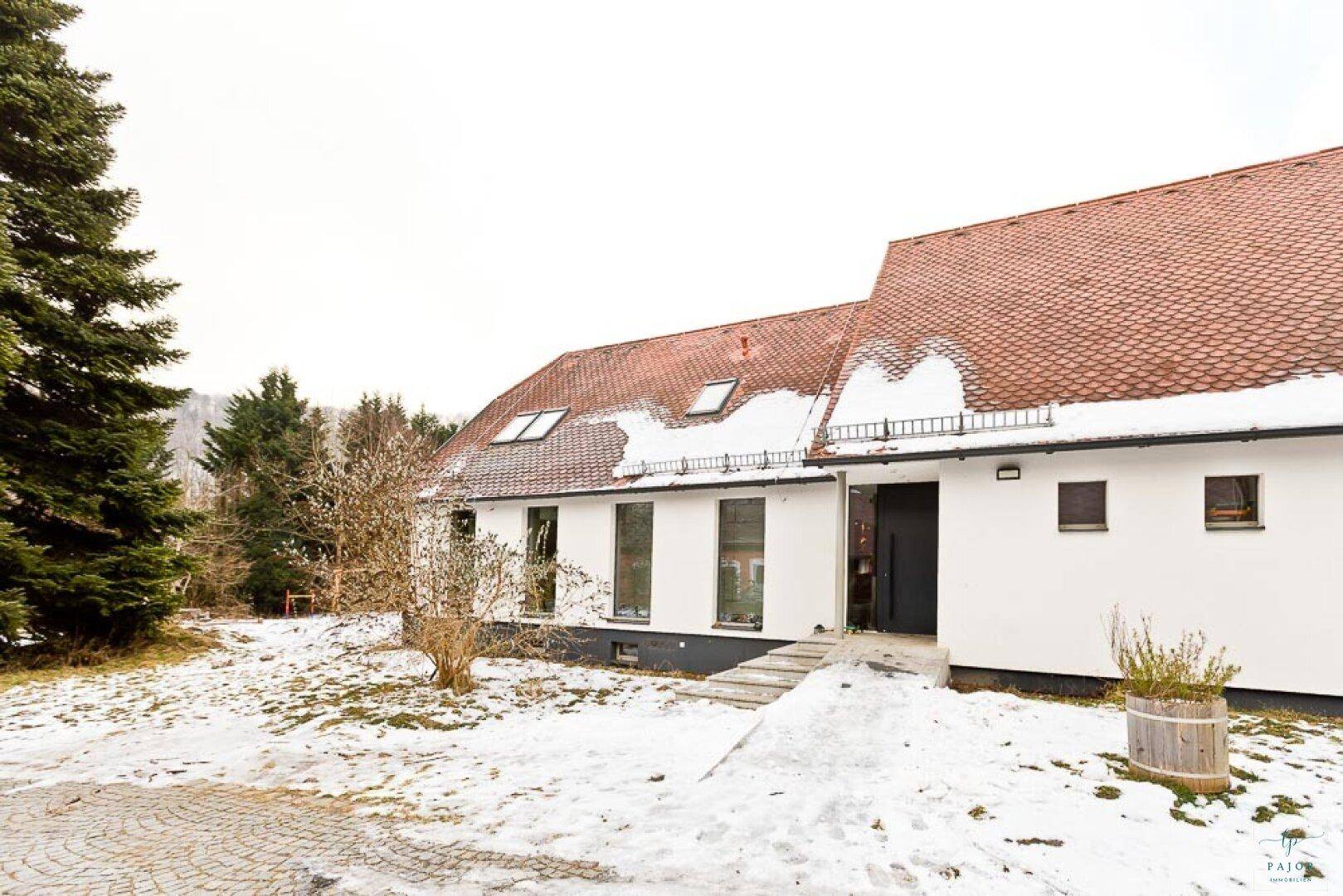Vorderansicht des weißen Hauses mit rotem Dach, Eingangsbereich und verschneitem Vorgarten.