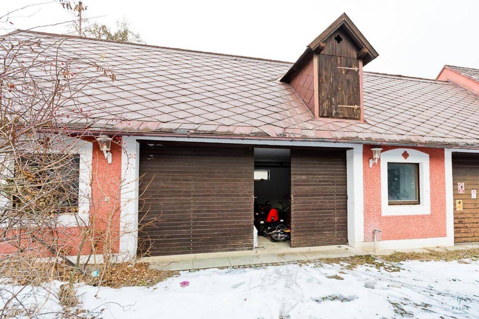 Rotes Gebäude mit zwei großen Holzgaragentoren und einem kleinen Dachgiebel.