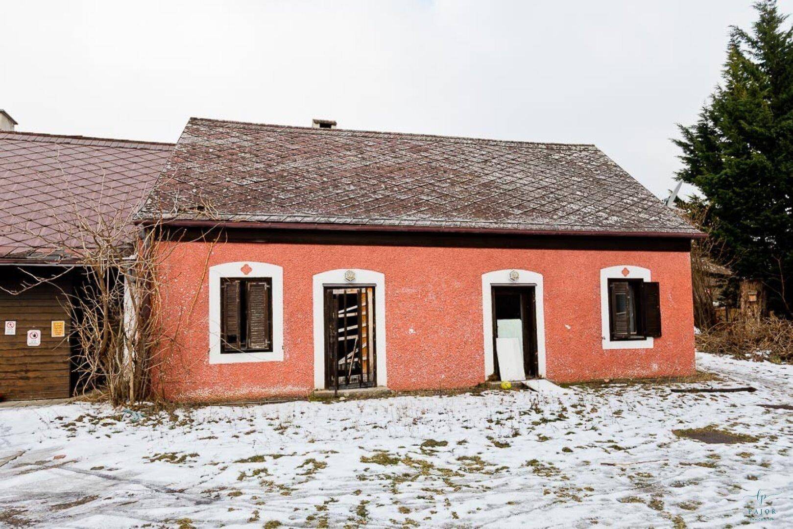 Altes rotes Gebäude mit mehreren Türen und Fenstern, umgeben von Schnee und Bäumen.