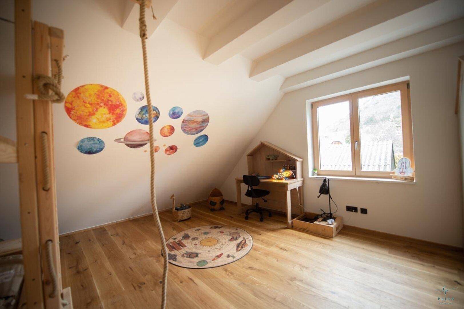 Helles Dachzimmer mit Schreibtisch, Holzboden und verspielten Planeten-Wanddekorationen.