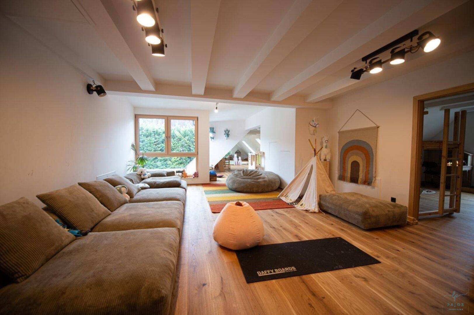 Gemütliches Wohnzimmer mit großem Sofa, Holzboden und sichtbaren Deckenbalken.