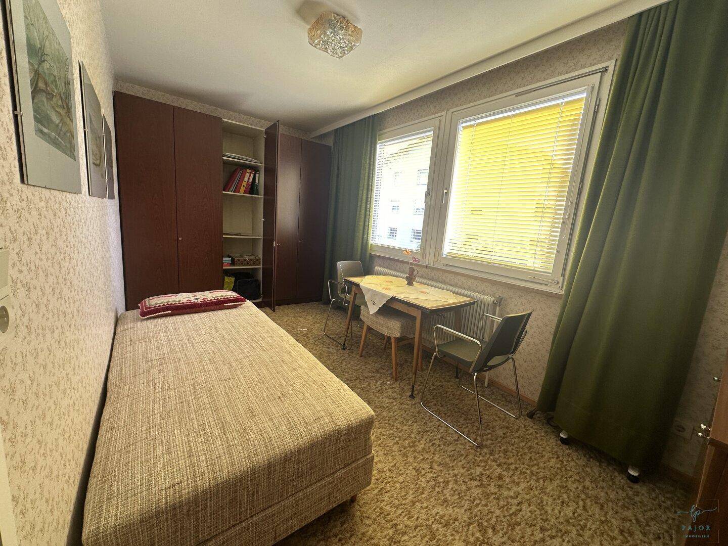 Kleines Schlafzimmer oder Gästezimmer mit Einzelbett, Tisch und Einbauschränken, hell durch Fenster.
