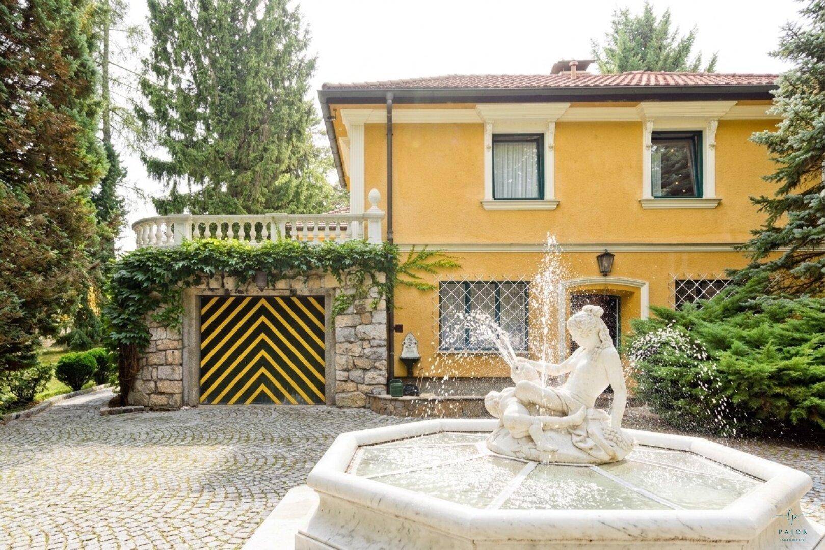Detailansicht der gelben Villa mit Springbrunnen und dekorativem Garagentor.