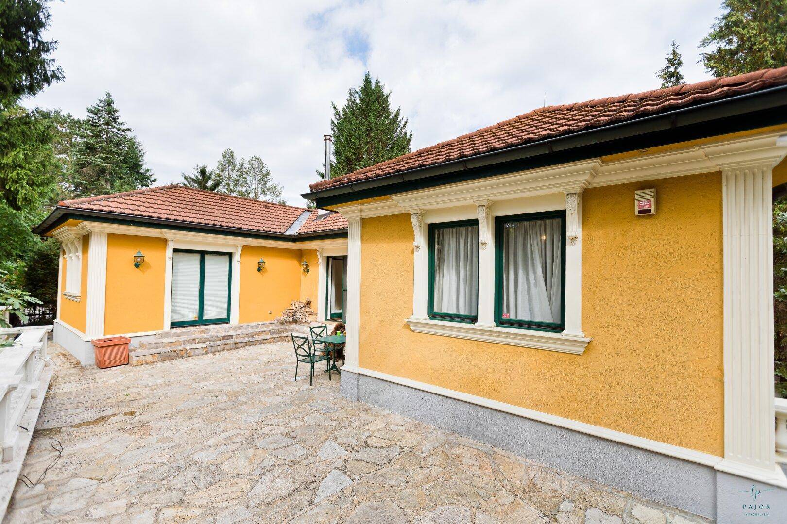 Weitläufige Steinterrasse entlang der gelben Villa mit Blick auf die grüne Umgebung.