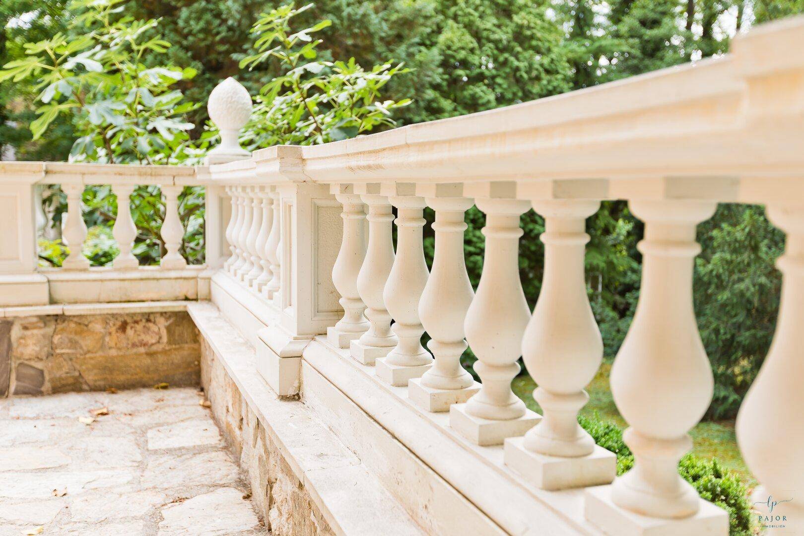 Elegante Balustrade aus hellem Stein mit Blick auf die grüne Gartenlandschaft.