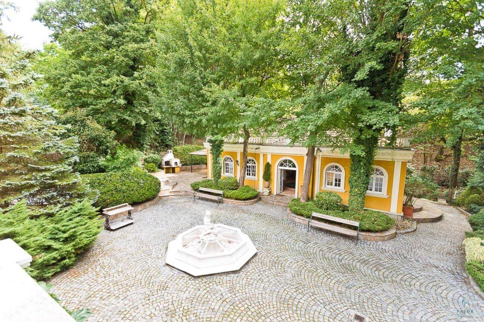 Vogelperspektive des Anwesens mit Springbrunnen, Nebengebäude und weitläufiger Gartenanlage.