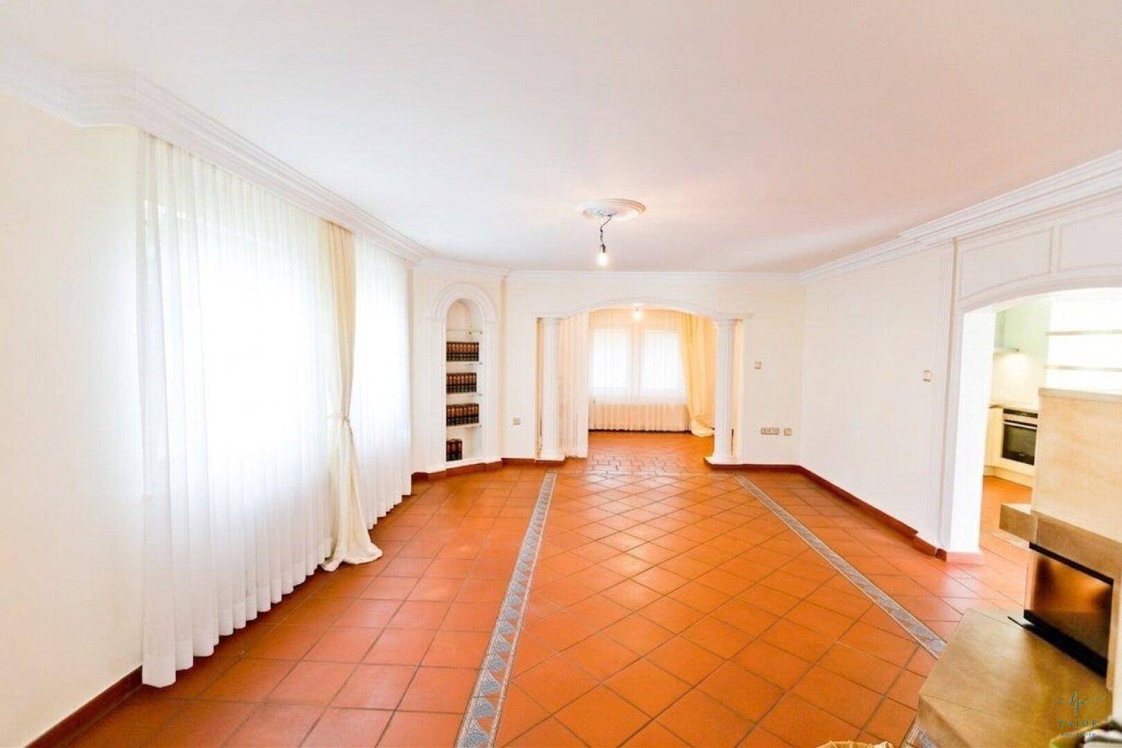Heller Wohnbereich mit Terrakottafliesen, großen Fenstern und Durchgängen zu angrenzenden Zimmern.