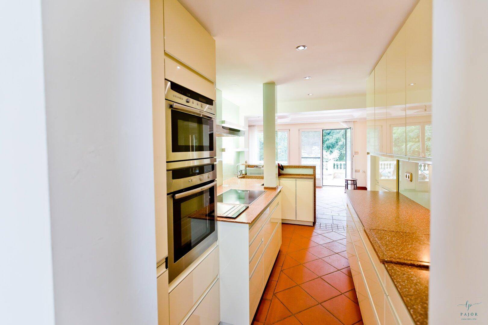 Moderne Küche mit integrierten Backöfen, Terrakottafliesen und Blick in den Wohnbereich.