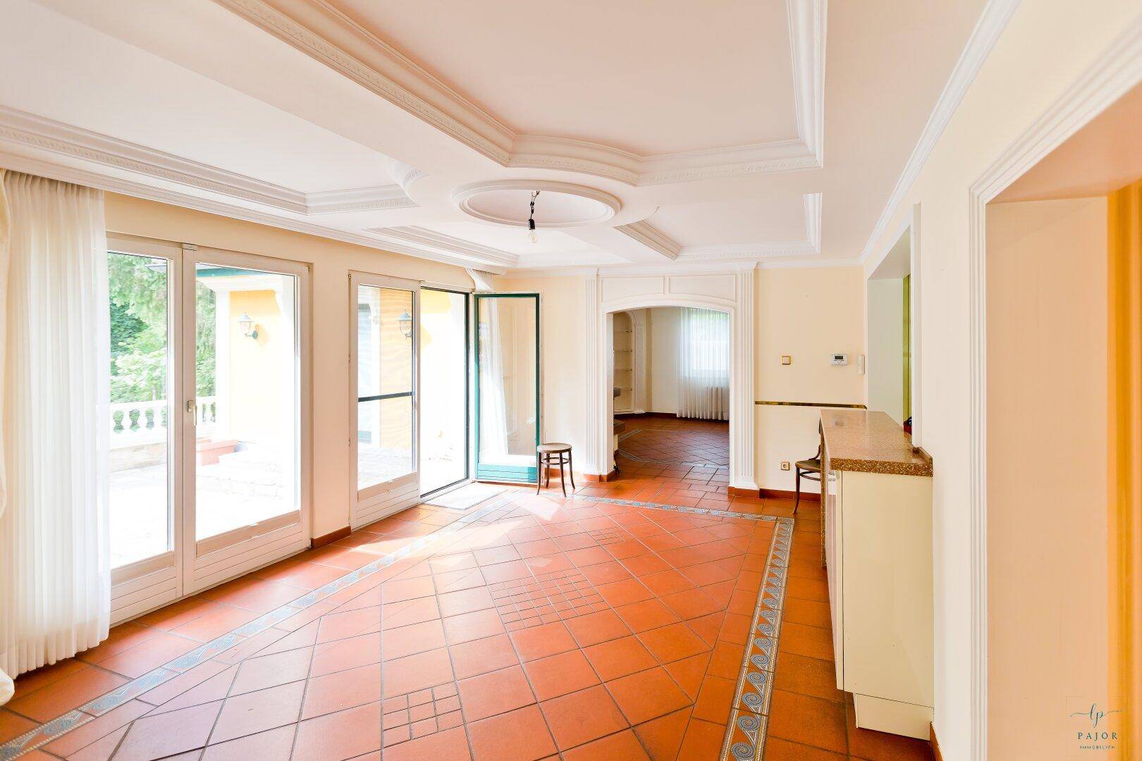 Geräumiges Wohnzimmer mit Terrakottafliesen, Stuckdecke und Zugang zur Terrasse.