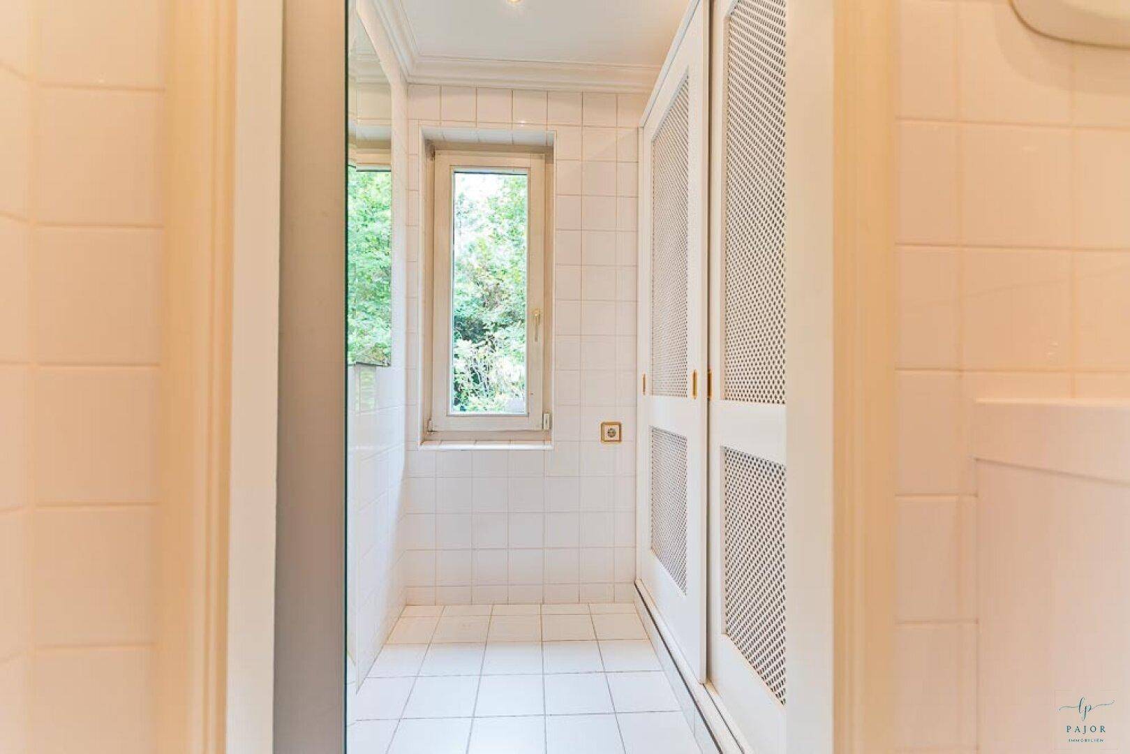 Heller Flur mit weiß gefliestem Boden, Fenster und integrierten Schränken.