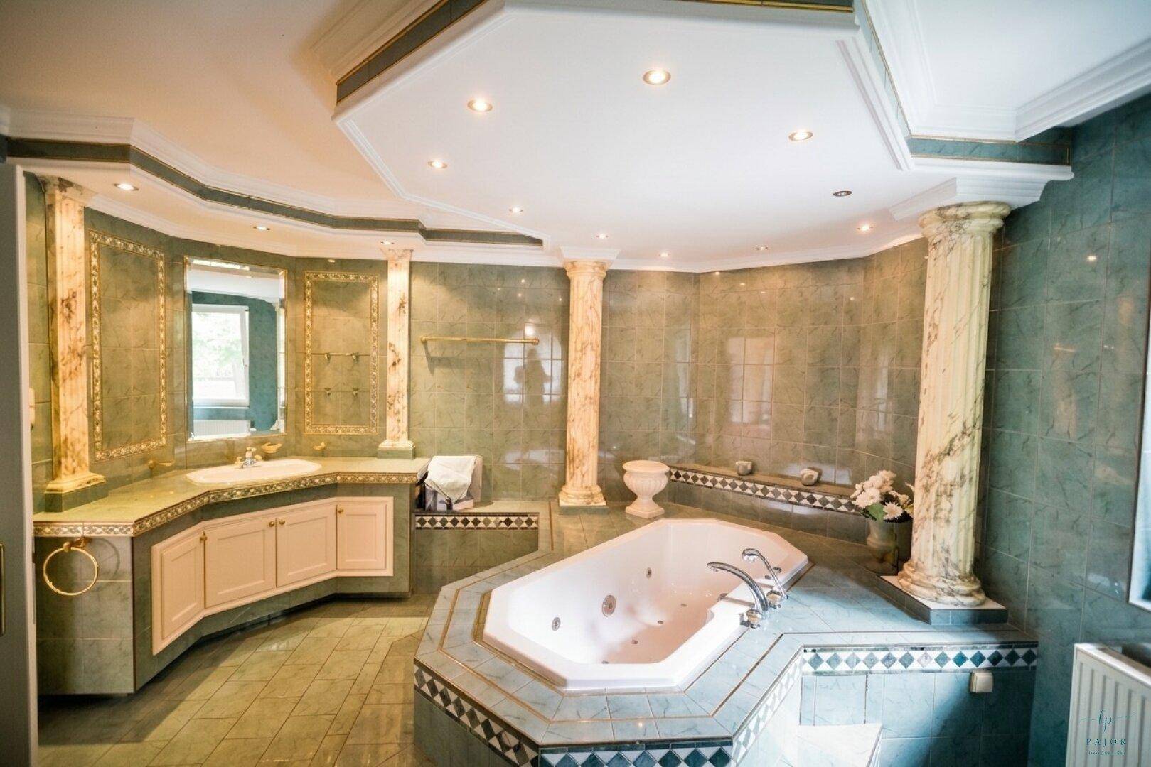 Luxuriöses Badezimmer mit Whirlpool-Badewanne, grünen Fliesen und dekorativen Säulen.
