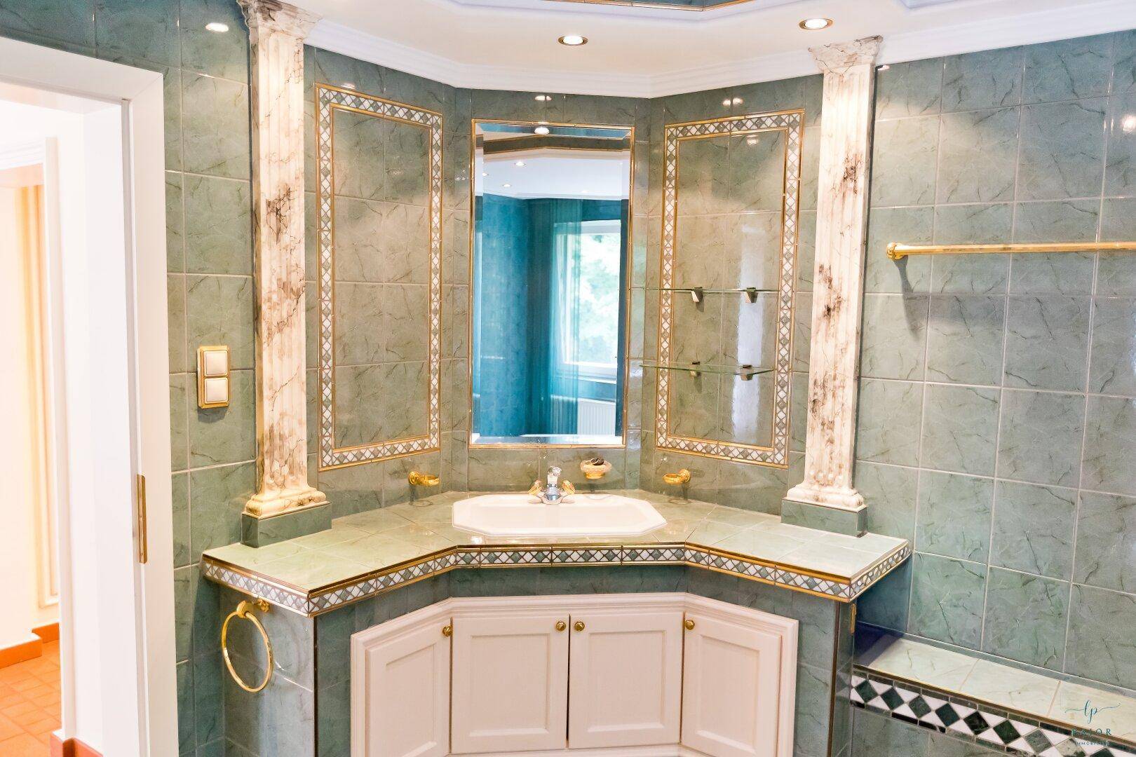 Elegantes Badezimmer mit Eckwaschbecken, großem Spiegel und grünen Marmorfliesen.