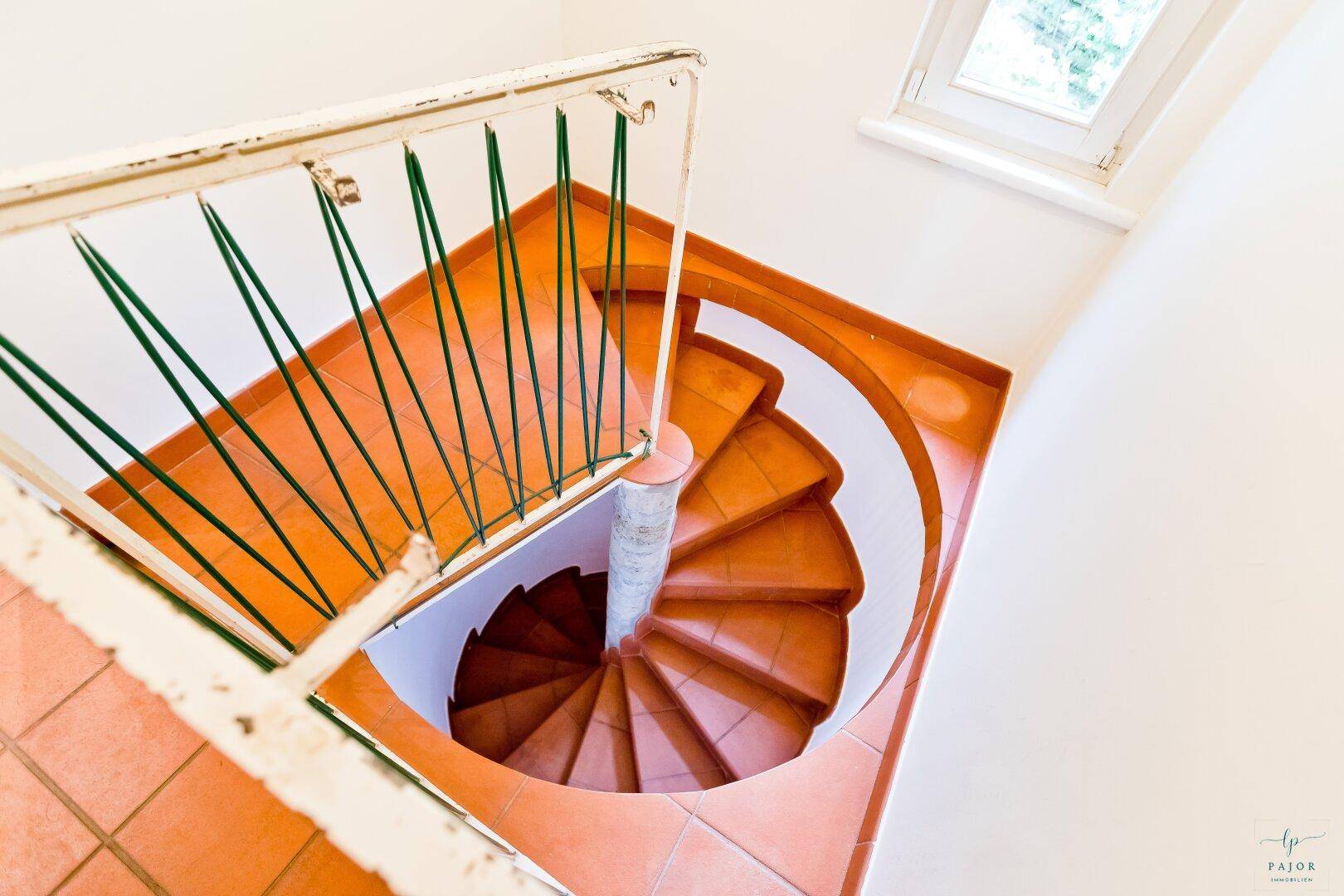 Wendeltreppe mit Terrakottafliesen und grünem Geländer, die verschiedene Ebenen verbindet.